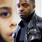 faisal-web Dr. Faisal Abdu'Allah portrait. Faisal is wearing a black turtleneck with a black leather jacket. He is in the forefront of the photo and behind him is a photograph of a half face of a young child.