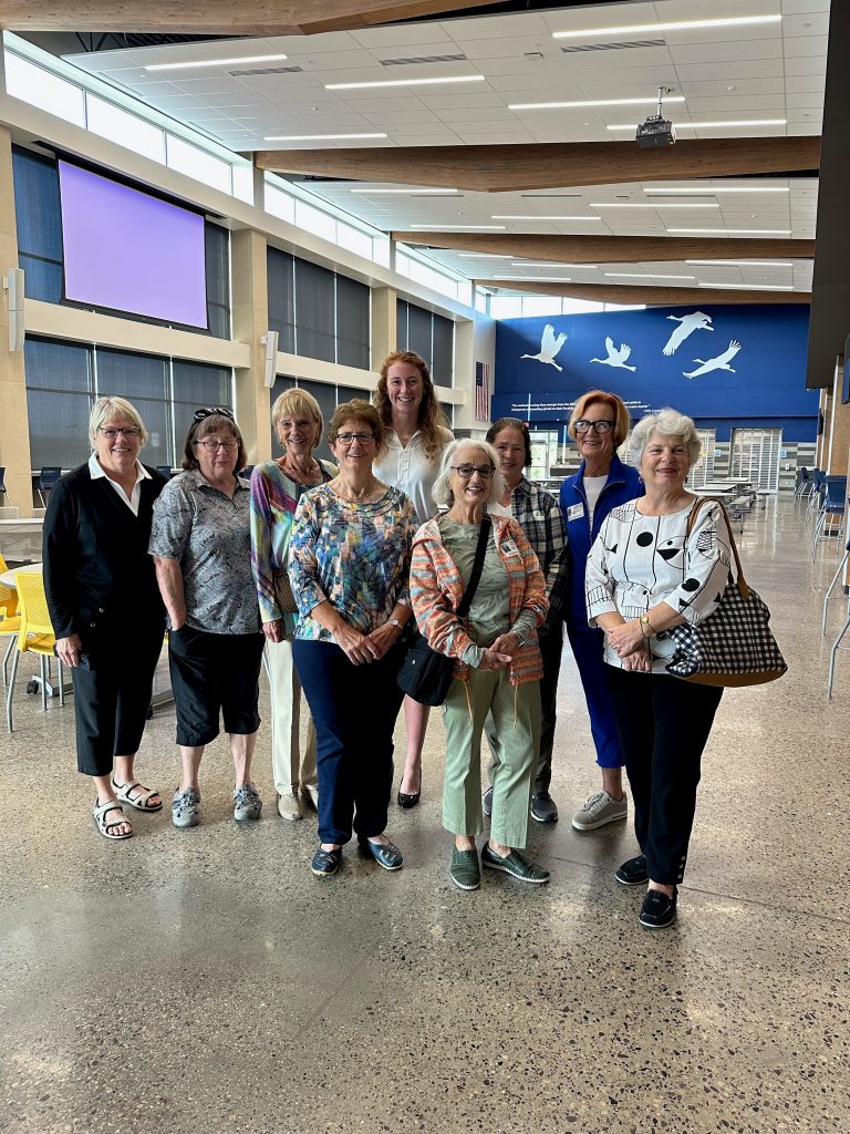 Kathy is standing posing with eight women. They are all smiling. There is three women in the front row and five women in the back row.