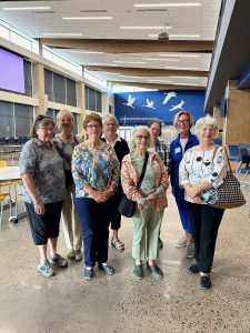 Kathy is standing posing with seven women. They are all smiling. There is three women in the front row and four women in the back row.