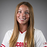 Erin Connolly Pictured is Erin Connolly. She is smiling. She has brown hair that is resting on he shoulders. She is wearing a white Wisconsin jersey.
