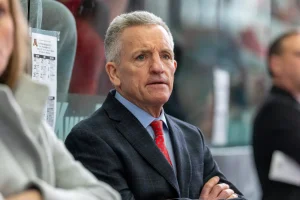 Photo of Coach Mark Johnson wearing a dark gray suit, light blue shirt, and red tie.