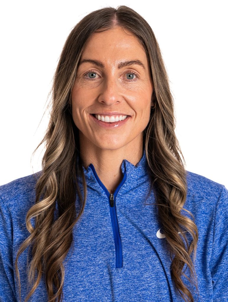 Professional athletic headshot of SMU tennis coach Kelcy McKenna smiling, wearing a blue heathered Nike quarter-zip pullover against a plain white background.