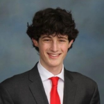 Joseph Corritone Headshot of Joseph Corritone, a smiling young man with dark curly hair wearing a dark gray suit, white shirt, and red tie against a studio backdrop.