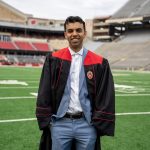 SGHeadshot Portrait of a smiling Suvir Grover on a football field, wearing a black graduation gown with red accents and a golden 'W' crest over a light blue suit.